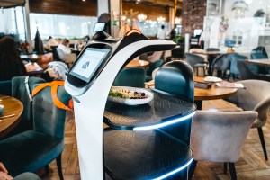 Restaurant kitchen with a burger-flipping robot alongside chefs preparing food.